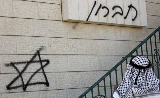A Palestinian man wearing the traditional chequered head scarf looks on December 2, 2008 at graffitti sprayed at the entrance of a mosque in the West Bank village of Sinjel, near Ramallah, by a group of Israeli settlers earlier in the day. The graffiti in Hebrew reads 