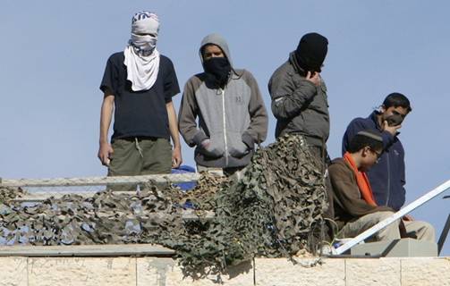 Masked Jewish settlers stand atop the roof of a disputed building, occupied by settlers in March 2007, in the West Bank city of Hebron, December 3, 2008. Hardline Jewish settlers have vowed to resist an Israeli court order to leave the building they insist they bought from a Palestinian. Hundreds of settler supporters, mostly youths, have come to the Jewish enclave in the past week to try to prevent the evacuation of the building, raising tensions. Palestinian Faiz Rajabi said the building belongs to him and he has denied selling it to the settlers. From Reuters Pictures by REUTERS.